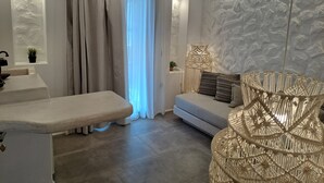Uma sala de estar moderna com um sofá, um banquinho, uma cadeira de vime e uma parede texturizada.