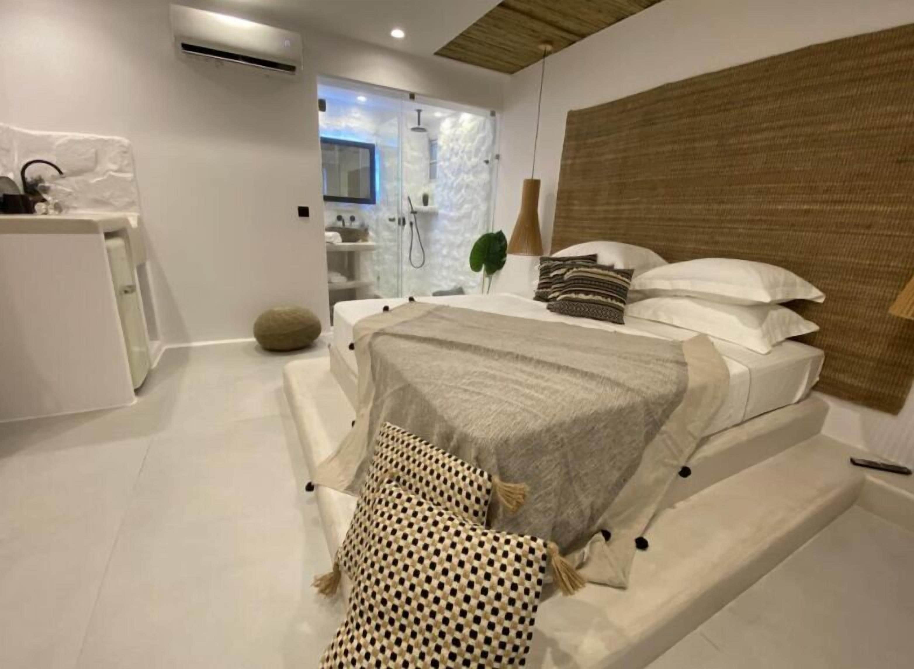 A modern bedroom with a large bed, a small desk, and a shower area.