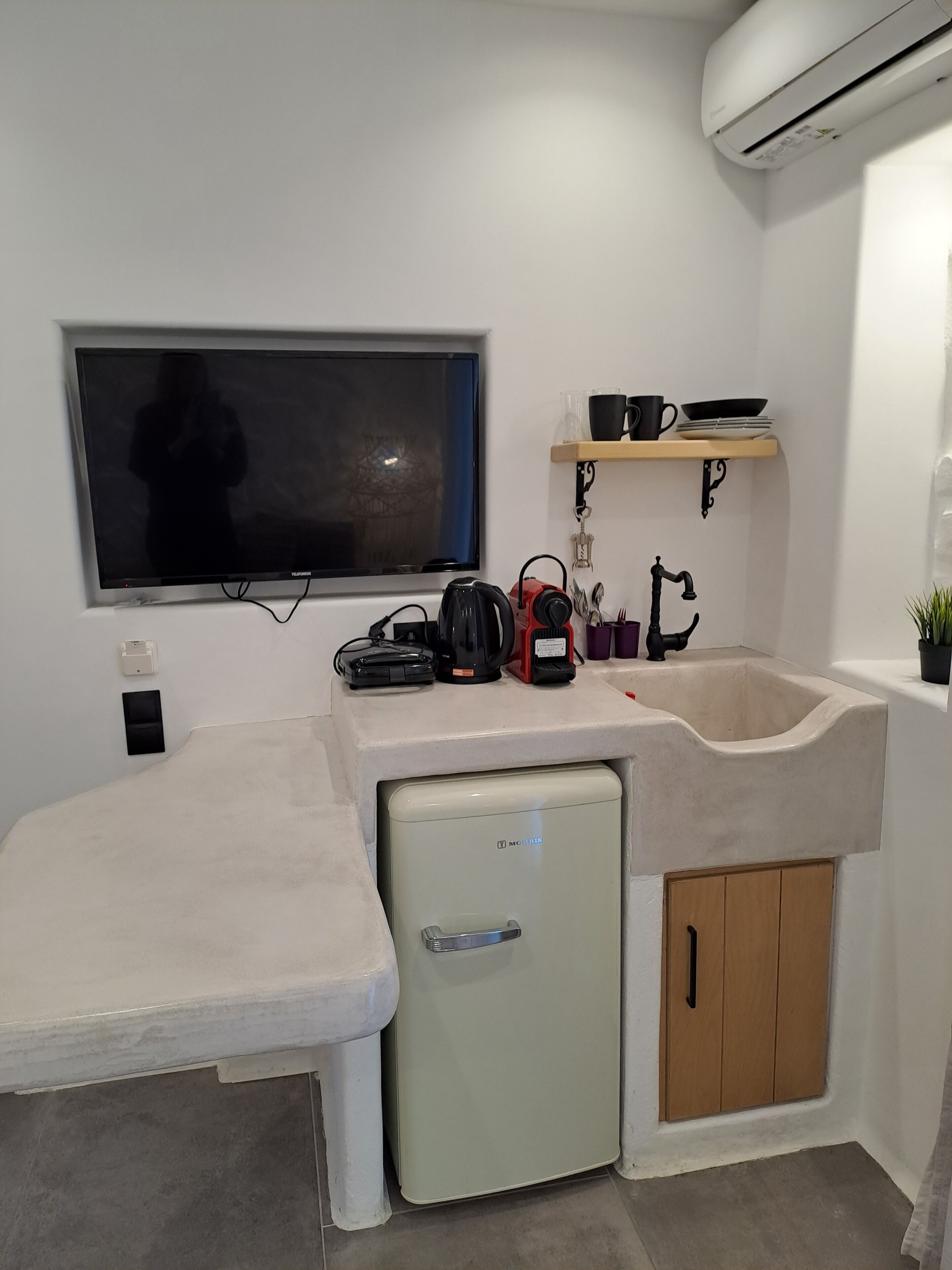 Una cocina compacta con un refrigerador integrado, un lavamanos y un televisor de pantalla plana montado en la pared.
