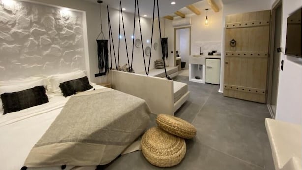 Quarto moderno com uma cama grande, um espaço de estar pequeno e uma cozinha ao fundo.