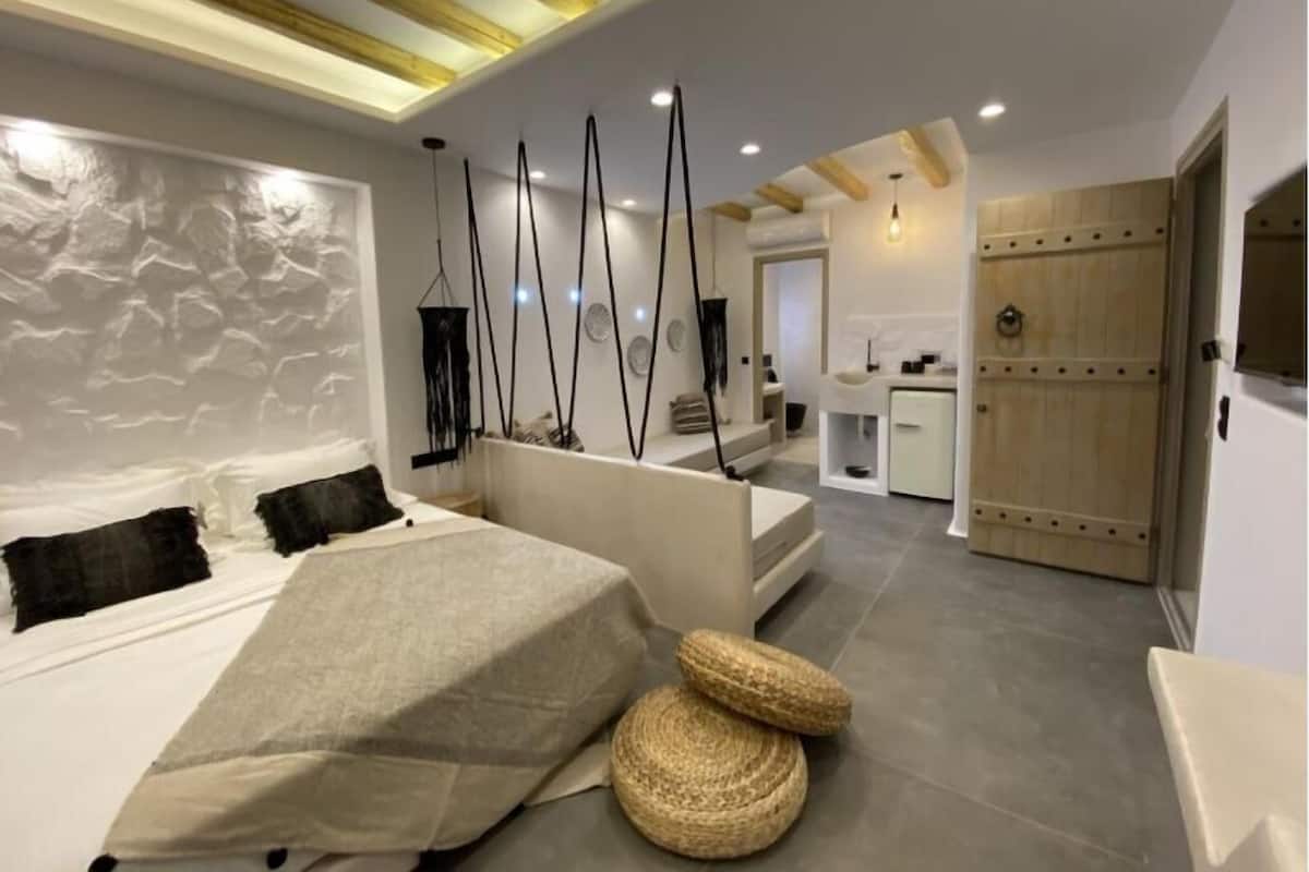 Une chambre moderne avec un grand lit, un petit coin salon et une cuisine à l’arrière-plan.