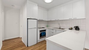 A modern kitchen with white cabinets, a built-in oven, a refrigerator, and a countertop with a kettle. - Modern and Spacious Three  Bedroom Apartment (Burwood)
