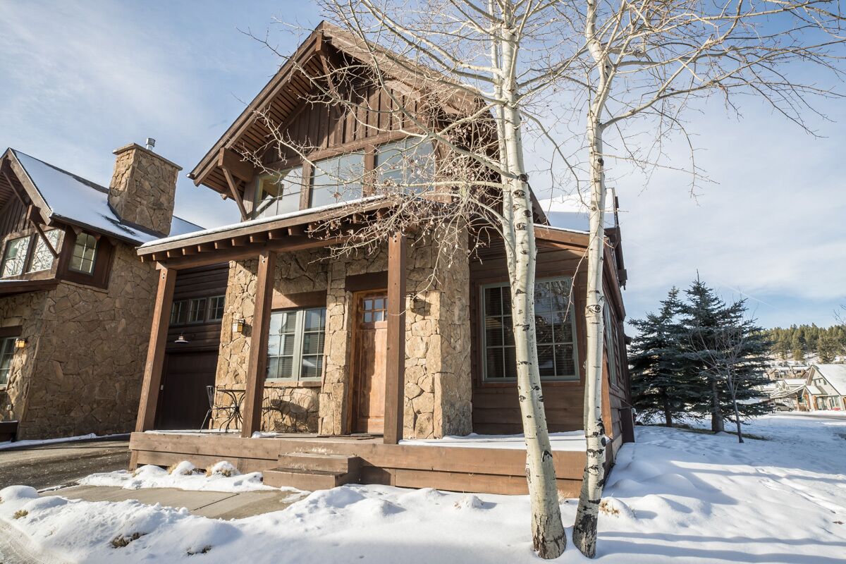 A stone and wood cabin with a stone chimney, large windows, and a wooden porch.