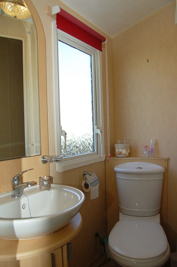 A bathroom with a sink, mirror, window, toilet, and a small shelf with toiletries.