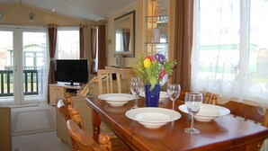 Comedor con mesa de madera para dos personas, televisor y un jarrón con flores.