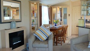 Una sala de estar acogedora con televisor, un sofá con almohada a rayas, una mesa de comedor para cuatro personas y una zona de cocina con armarios y encimera.