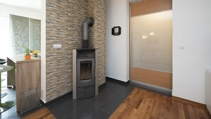A modern kitchen with a built-in wood-burning stove, a dining area with bar stools, and a glass door leading to another room. - Holiday Home Elijah Creek (Klis)