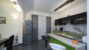 A modern kitchen with a green island, stainless steel appliances, and a black bar stool. - Holiday Home Elijah Creek (Klis)