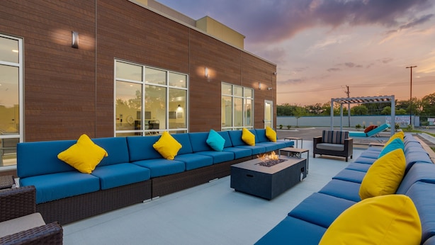 An outdoor seating area with blue and yellow cushions, a fire pit, and a pergola.
