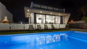 Ein modernes Haus mit Swimmingpool, Liegestühlen und einem gut beleuchteten Innenraum.