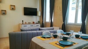 Ein modernes Wohnzimmer mit einer Sofagarnitur, einem Esstisch für vier Personen und einem wandmontierten Flachbildfernseher.