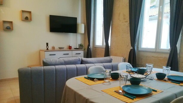 A modern living room with a sofa set, a dining table set for four, and a flat-screen TV mounted on the wall. - Gîte de la cathédrale in downtown Lectoure (Lectoure)
