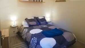 A neatly made bed with a patterned blanket, two bedside lamps, a small shelf with decorative items, and a window with a view of the sky. - Gîte de la cathédrale in downtown Lectoure (Lectoure)