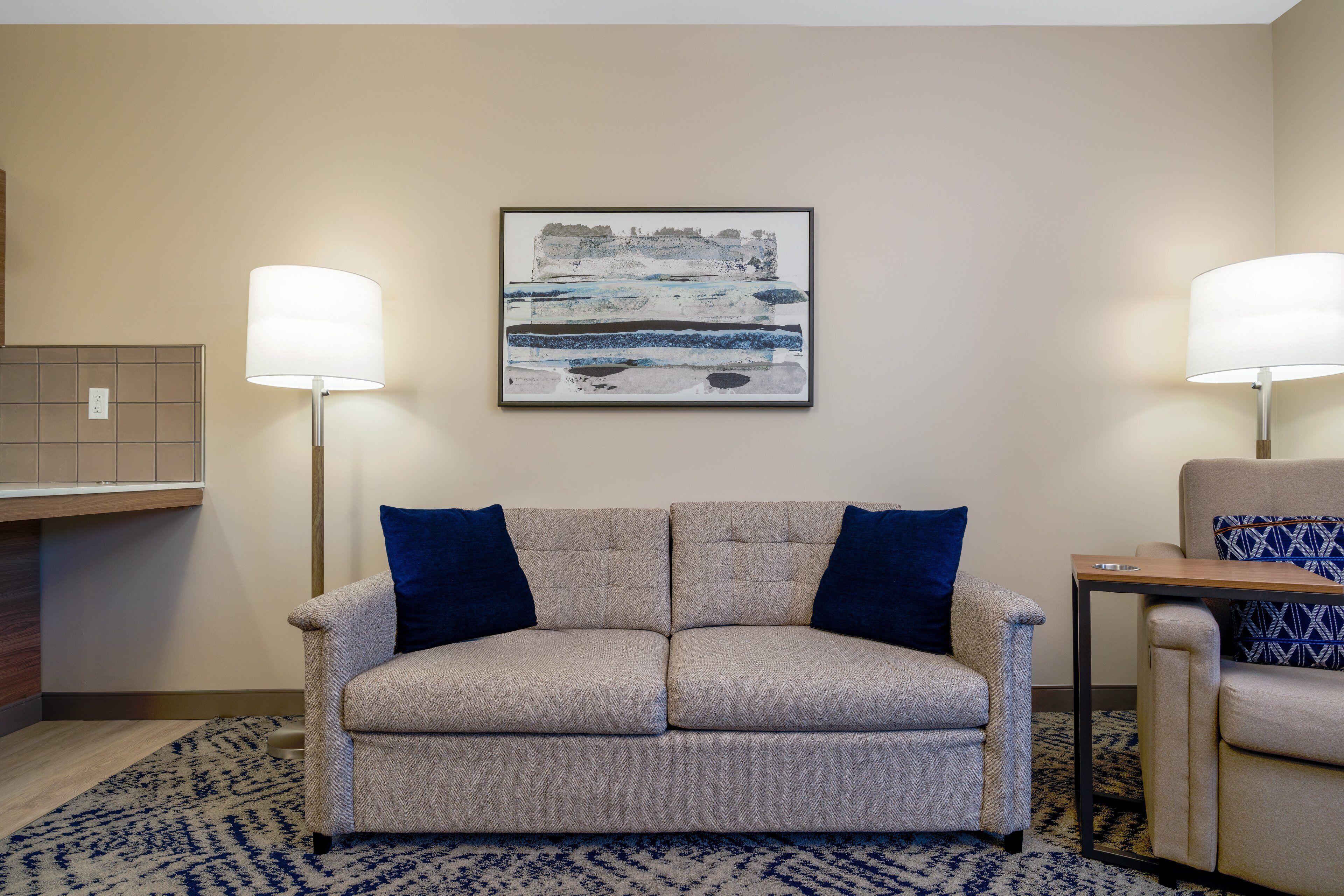 Ein Hotelzimmer mit einer Couch, einem kleinen Tisch, zwei Lampen und einem Wandbild.