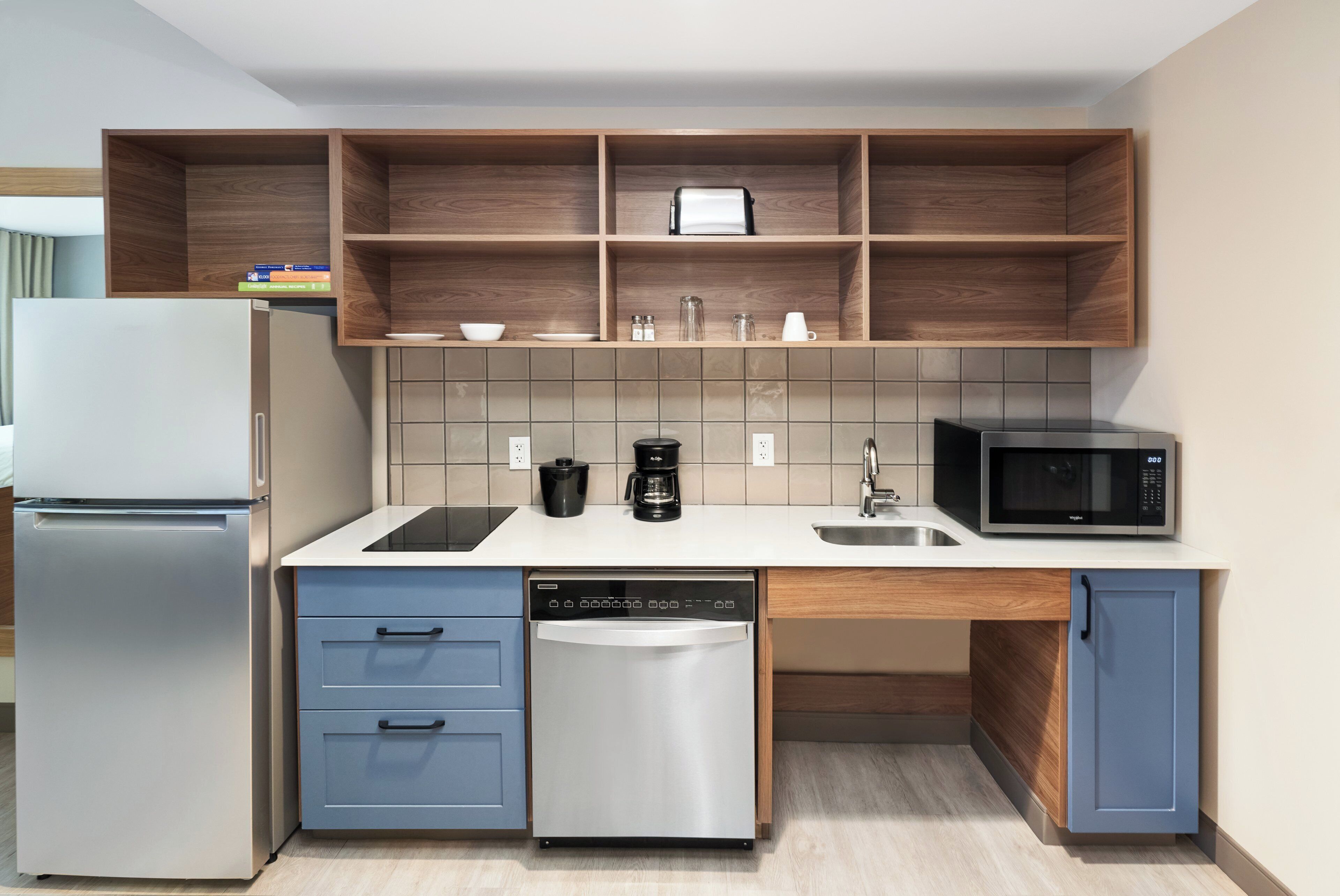 Cocina compacta equipada con refrigerador, lavavajillas, microondas y cafetera.