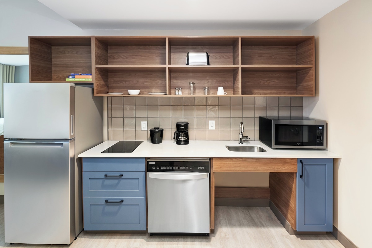 Cocina compacta equipada con refrigerador, lavavajillas, microondas y cafetera.