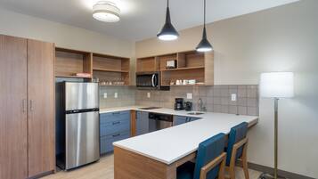 A modern kitchen with a stainless steel refrigerator, wooden cabinets, a white countertop, and blue bar stools.