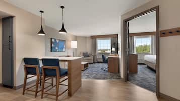 Habitació d'hotel amb cuineta, zona de menjador amb dues cadires, llit, escriptori amb un ordinador i una finestra gran.