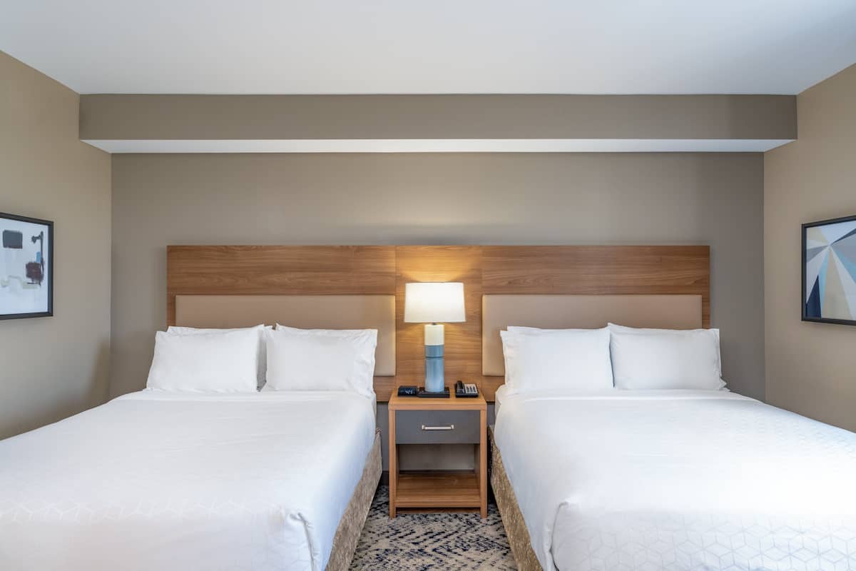 Une chambre d’hôtel avec deux lits, une table de chevet avec une lampe et un petit tiroir.