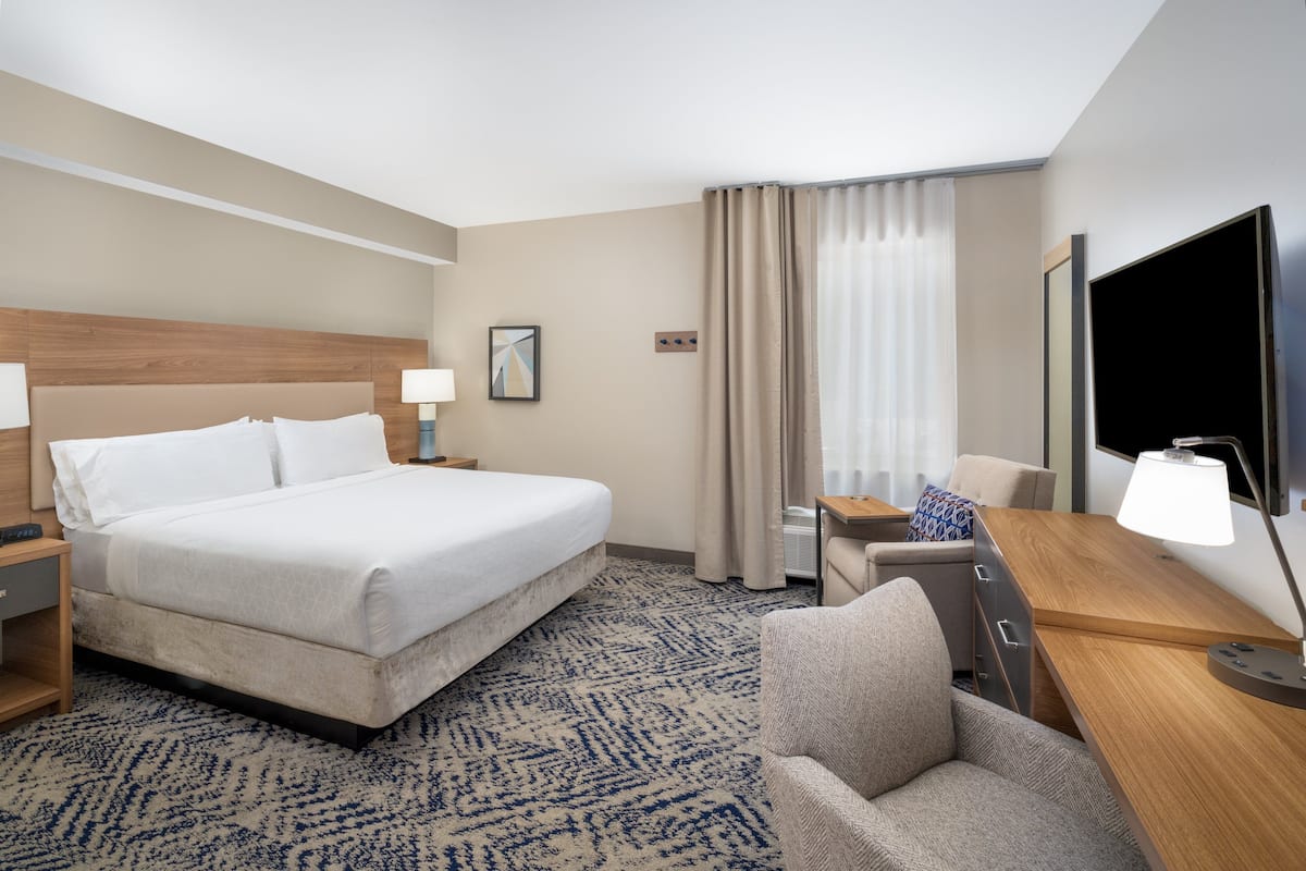 Une chambre d’hôtel avec un grand lit, un bureau avec une chaise, un téléviseur à écran plat et une fenêtre avec des rideaux.