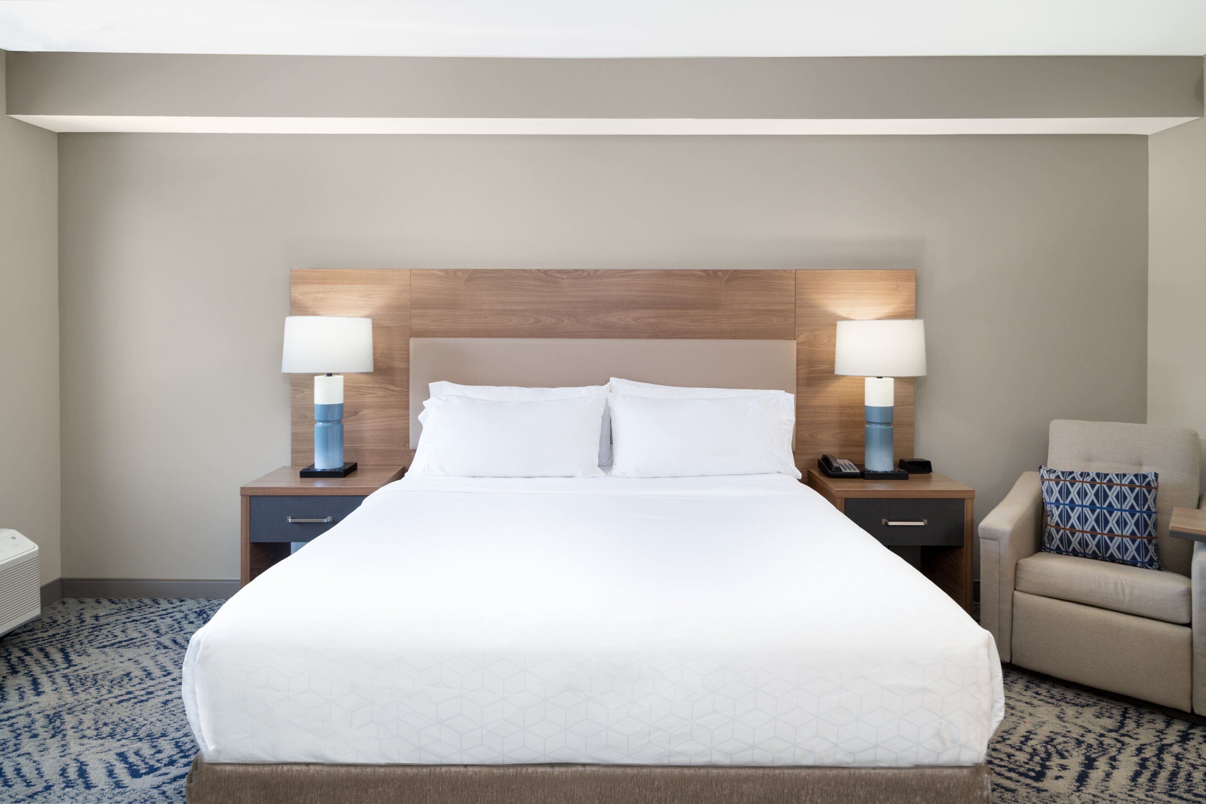 A hotel room with a large bed, two bedside tables with lamps, a chair, and a headboard.