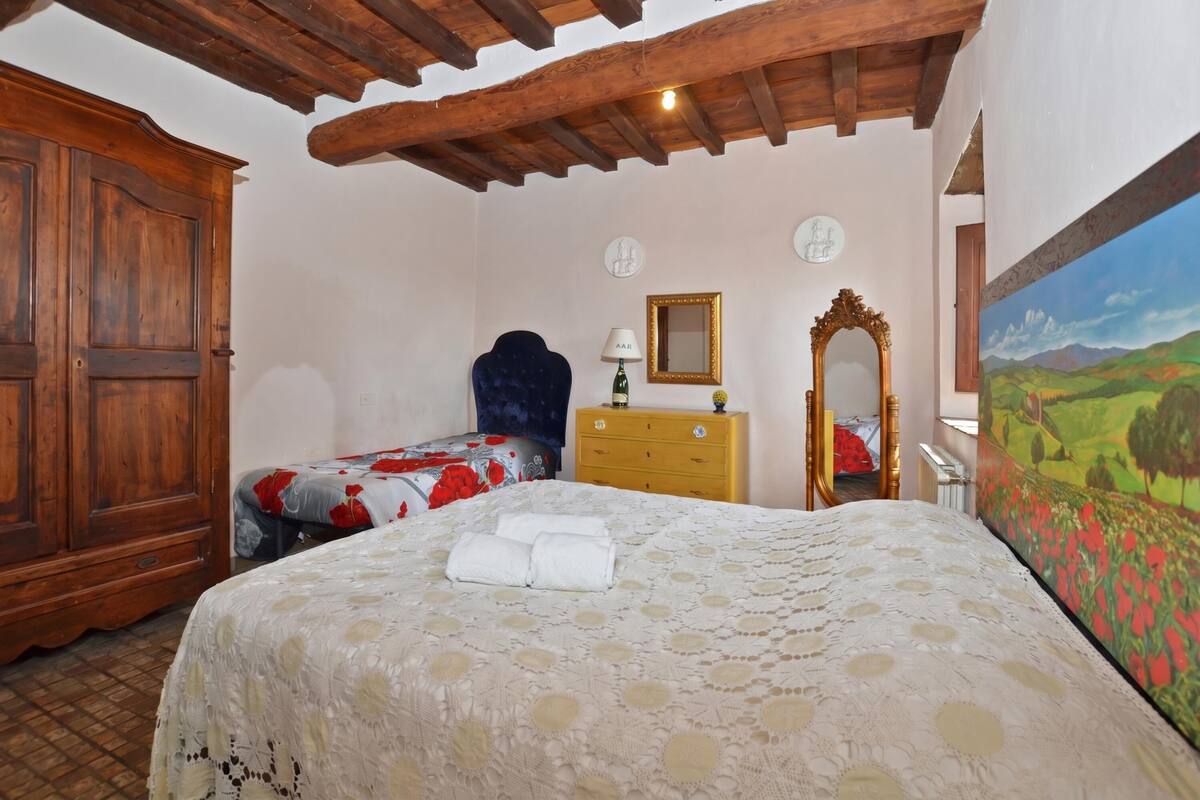 A bedroom with a wooden ceiling, a bed with a floral bedspread, a dresser, a mirror, and a painting on the wall.