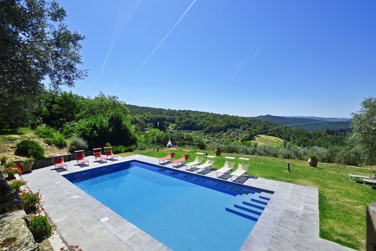 A swimming pool with lounge chairs, surrounded by a landscaped garden and a view of a hilly landscape.