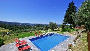 Una piscina rectangular con superficie de agua azul cristalina, rodeada por una solana pavimentada con tumbonas rojas y blancas.