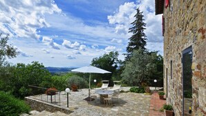 Un patio de piedra con una mesa, sillas y una sombrilla, con vistas al paisaje.