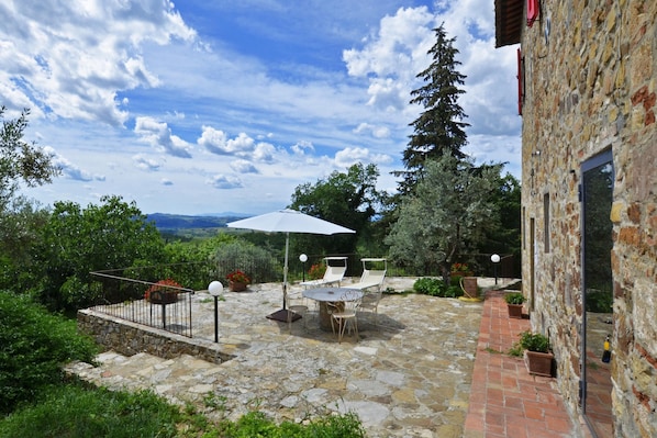 A stone patio with a table and chairs, an umbrella, and a view of the landscape.