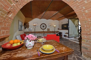 Un coin repas agrémenté d’une arche en briques, d’une table mise avec des assiettes, d’un vase rempli de fleurs et d’un panier de fruits.