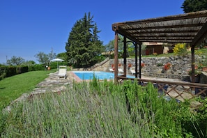 Uma área de piscina com pergolado, degraus de pedra e gramado.