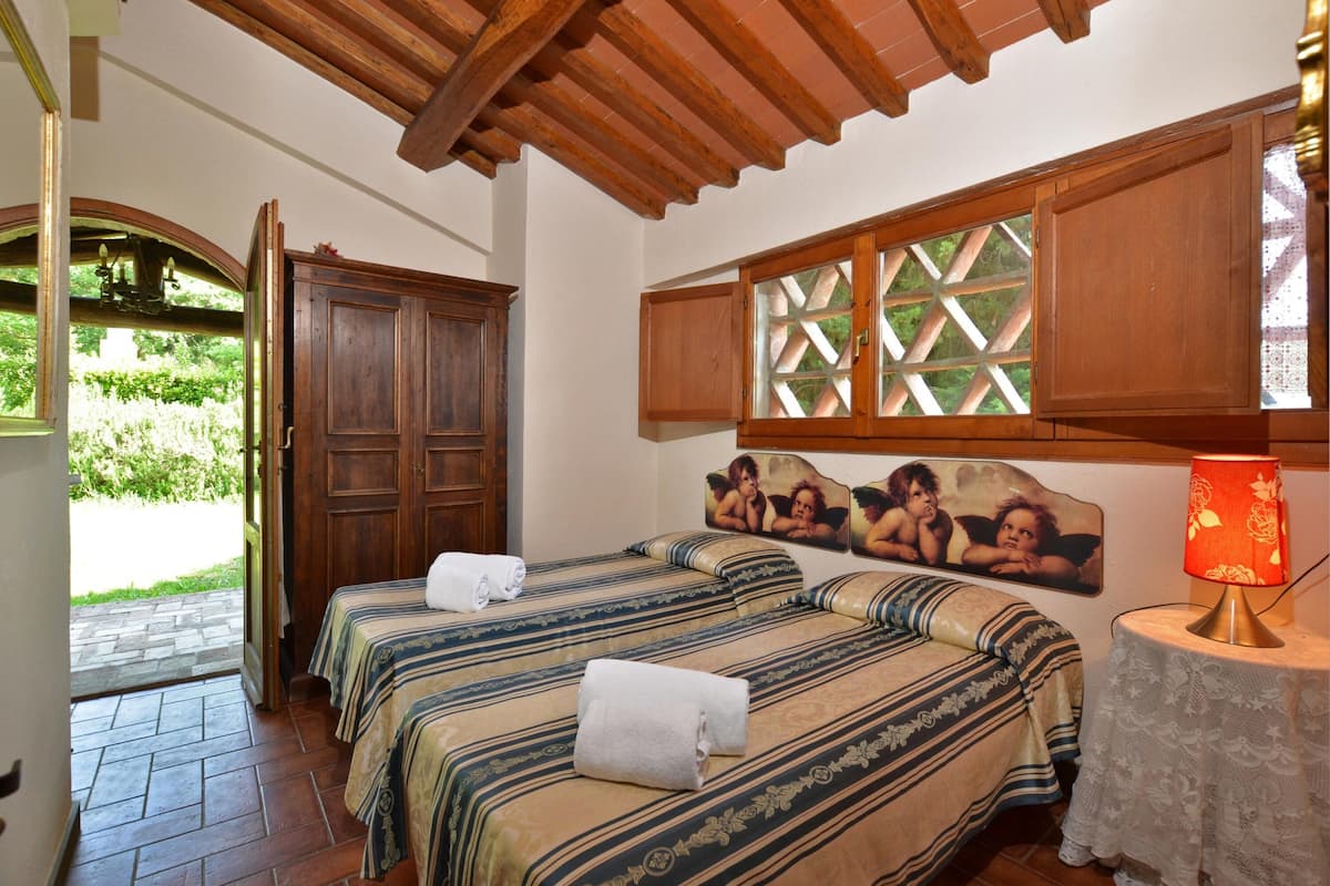 A room with two beds, wooden cabinets, a table with a lamp, and a window with a lattice design.