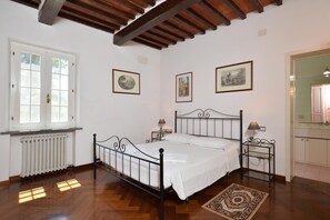 Quarto com piso de madeira, uma cama, radiador, janela e quadros nas paredes.