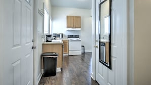 A narrow hallway with white doors, a trash bin, a microwave, a stove, and wooden cabinets.