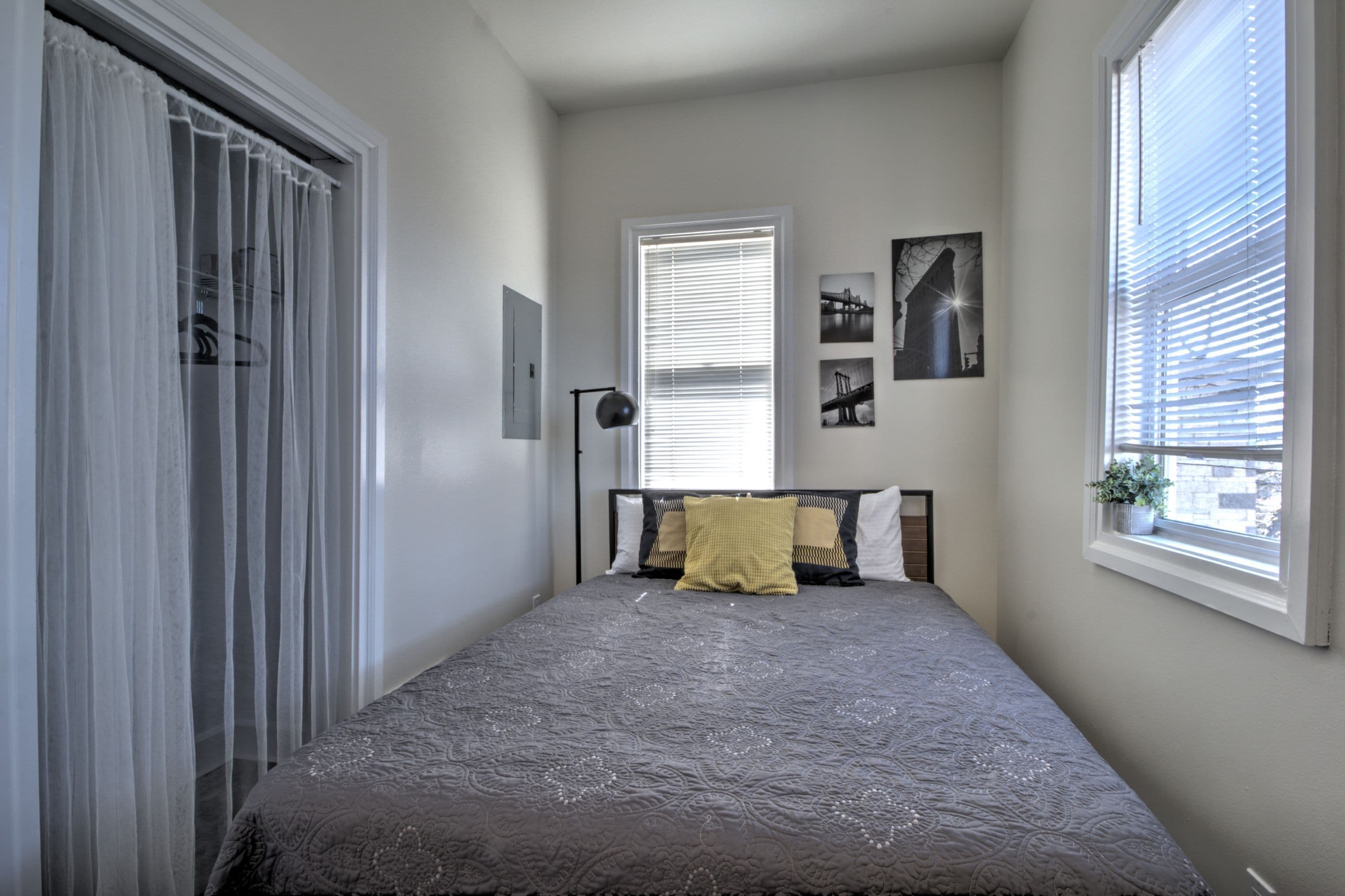 A bedroom with a bed, a window with blinds, a bedside lamp, and a wall-mounted picture.