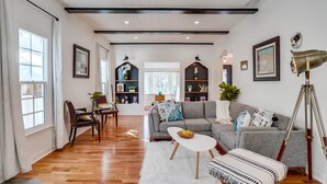 A spacious living room with a wooden floor, a grey sofa, a white coffee table, and a dining area with a wooden table and chairs.