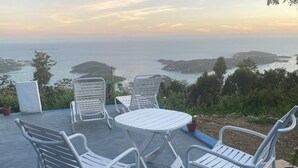 Une terrasse dotée d’une table ronde et de quatre chaises, offrant une vue sur un paysage côtier avec des îles et la mer.