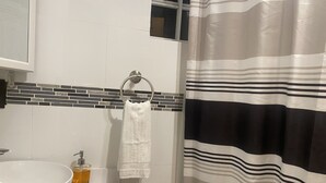 Une salle de bain avec un lavabo blanc, un verre contenant un liquide ambré, une serviette blanche suspendue à un anneau métallique et un rideau de douche à rayures.