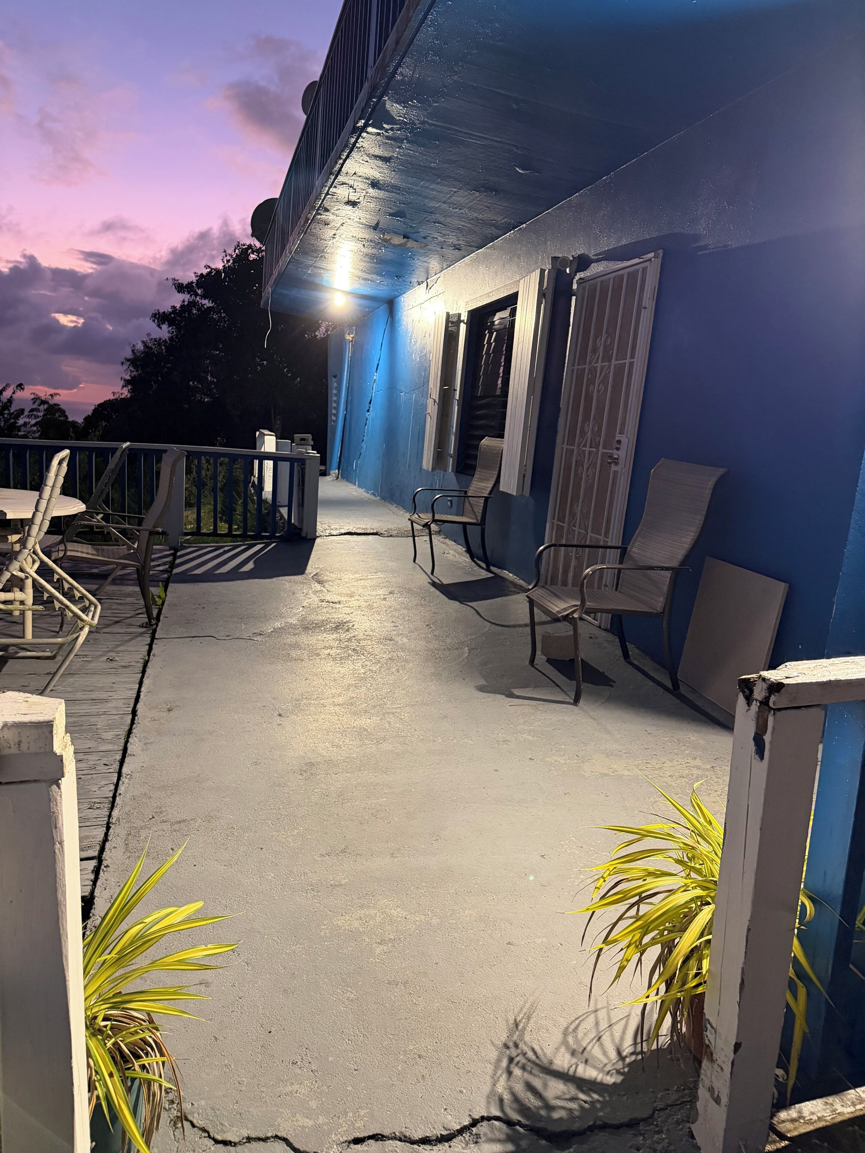 Un espace extérieur abrité, avec un mur bleu, deux chaises, une table et une plante en pot.