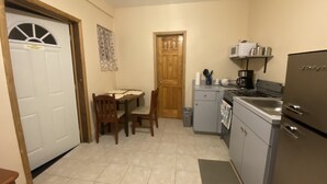 Une cuisine compacte équipée d’un réfrigérateur, d’une cuisinière et d’un évier. On y trouve une table à manger avec des chaises, ainsi qu’une porte avec une fenêtre.
