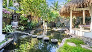 A tranquil garden with a pond, stone steps, and a thatched-roof structure. - The Village of Angels (Manggis)