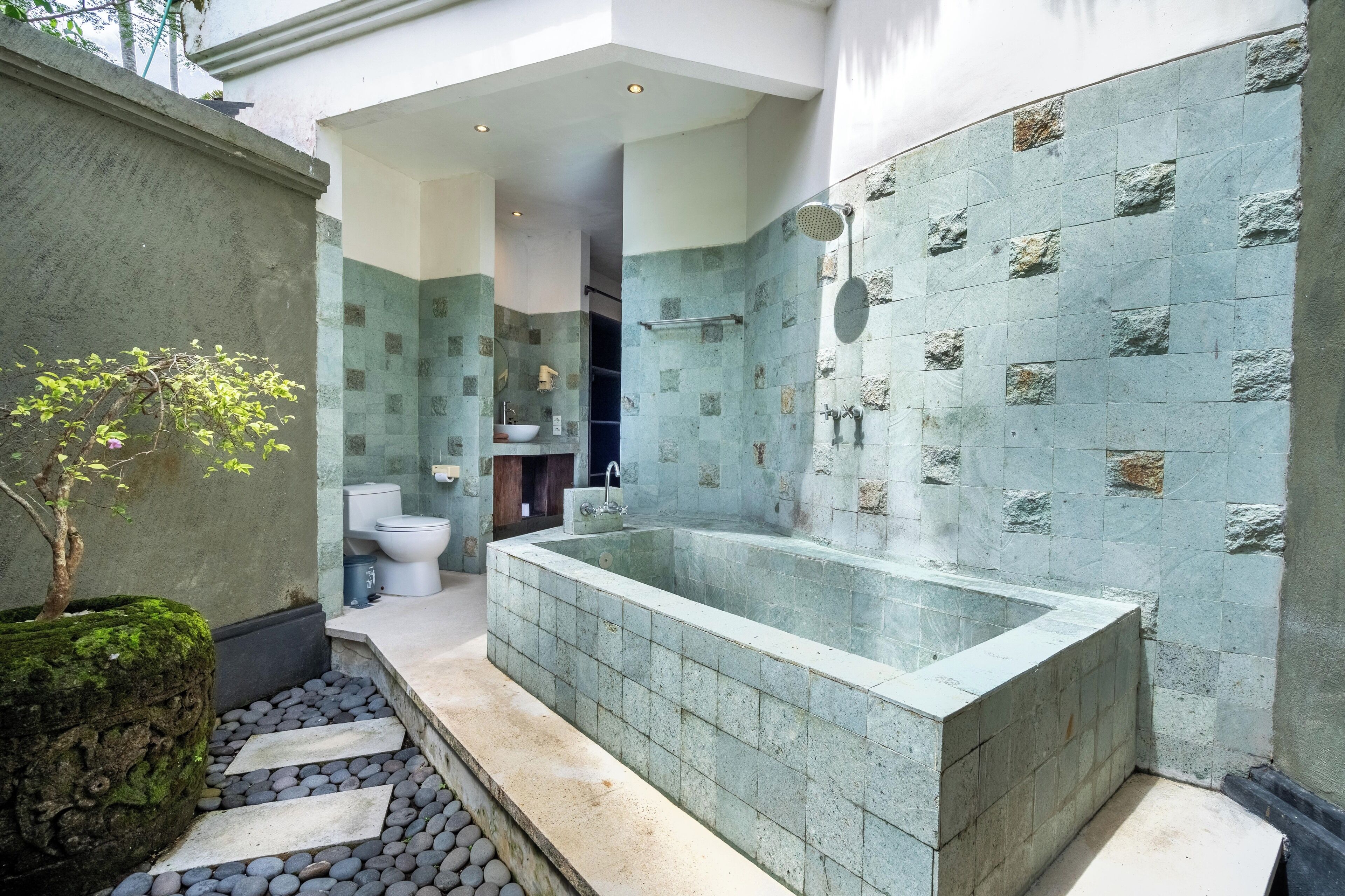 A modern bathroom with a freestanding bathtub, stone mosaic walls, and a small potted plant.