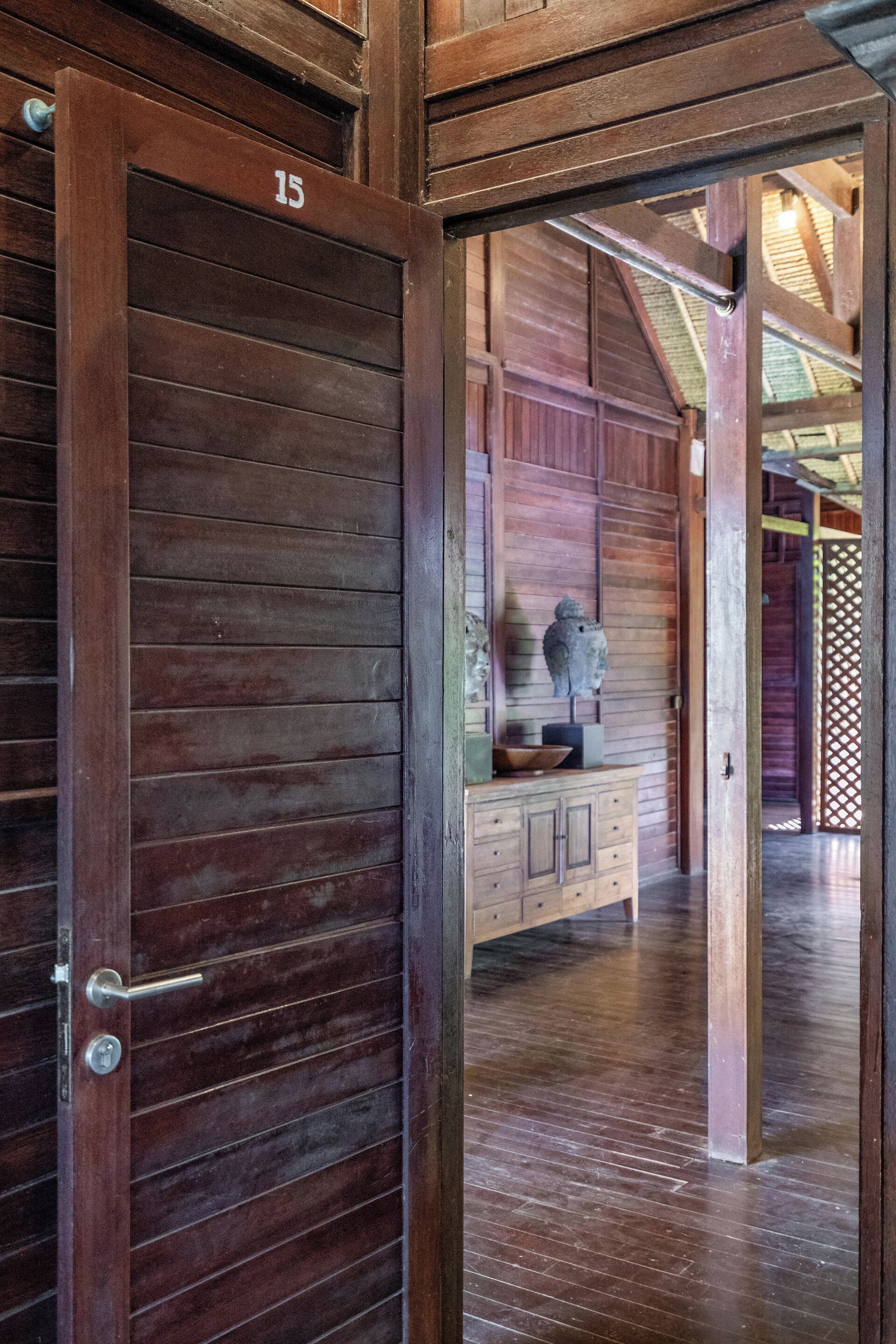 A wooden door with the number 15, leading into a room with a wooden floor and a cabinet with a bust sculpture.