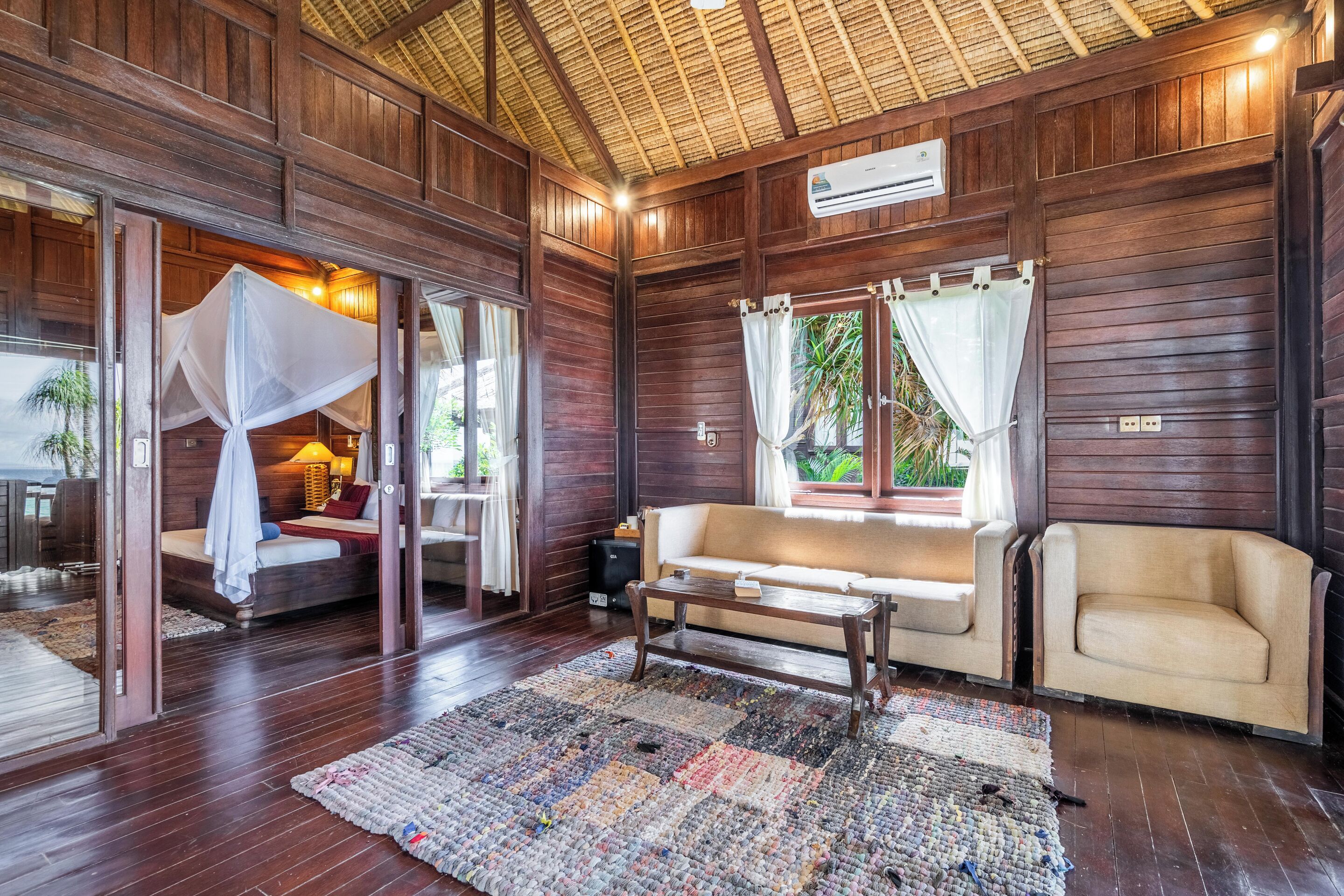 A wooden interior with a bed, sofa, and a large rug.