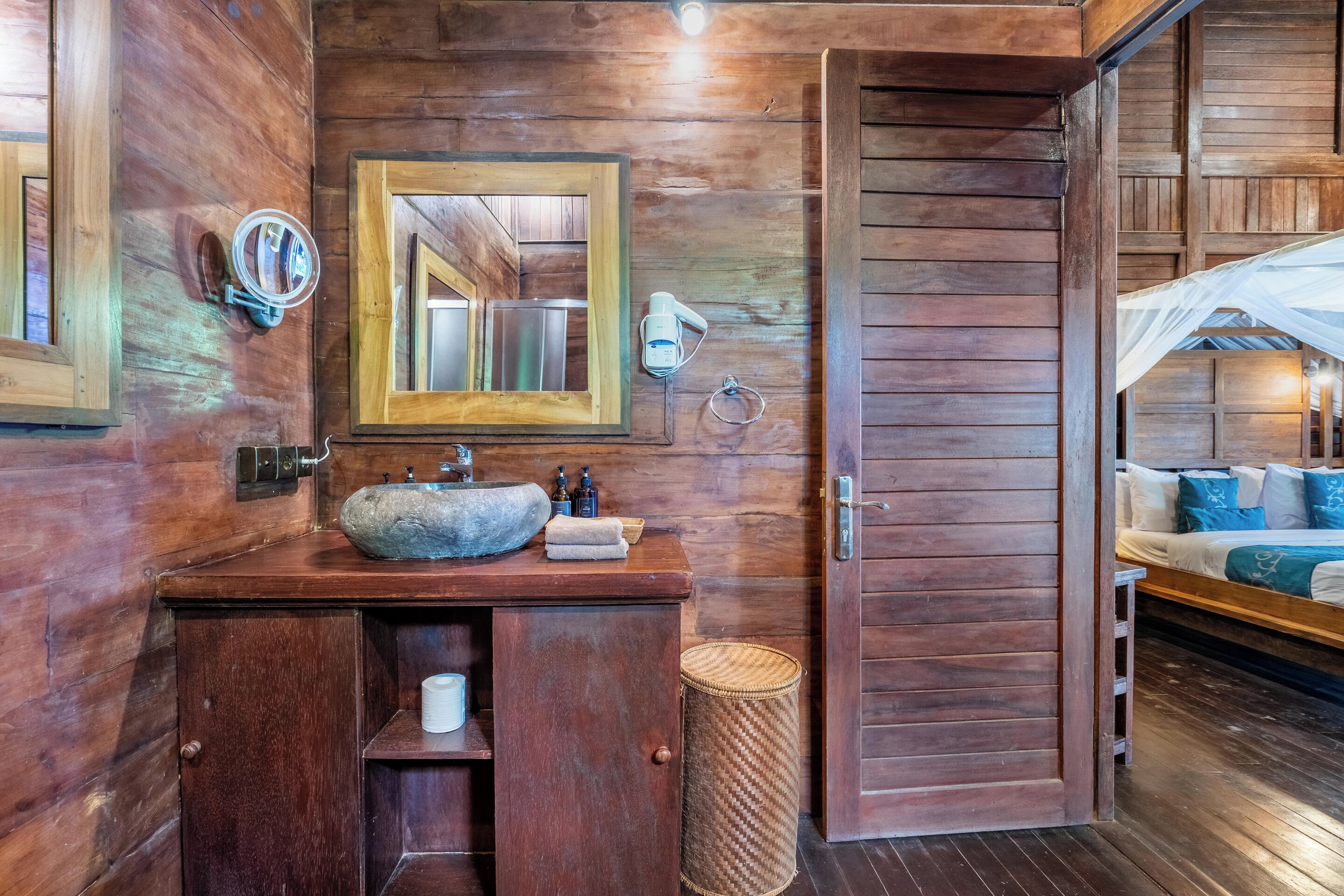 A wooden bathroom with a large mirror, a stone sink, and a wooden cabinet.