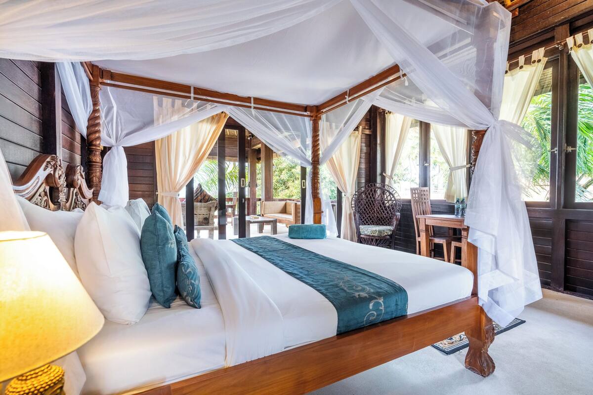 A bed with a canopy, a lamp, and a view of the outdoors.