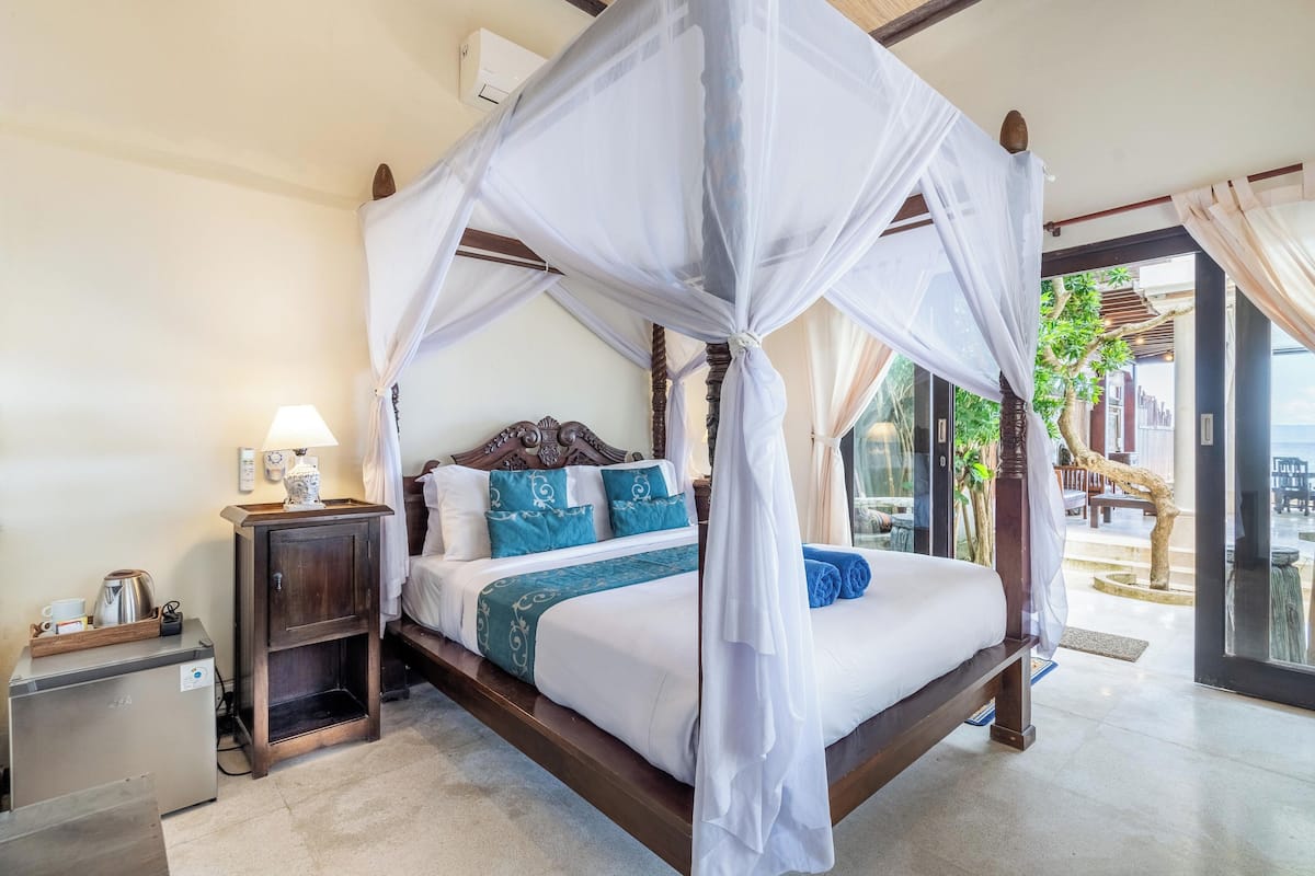 A four-poster bed with a canopy, a bedside table with a lamp, and a small refrigerator.
