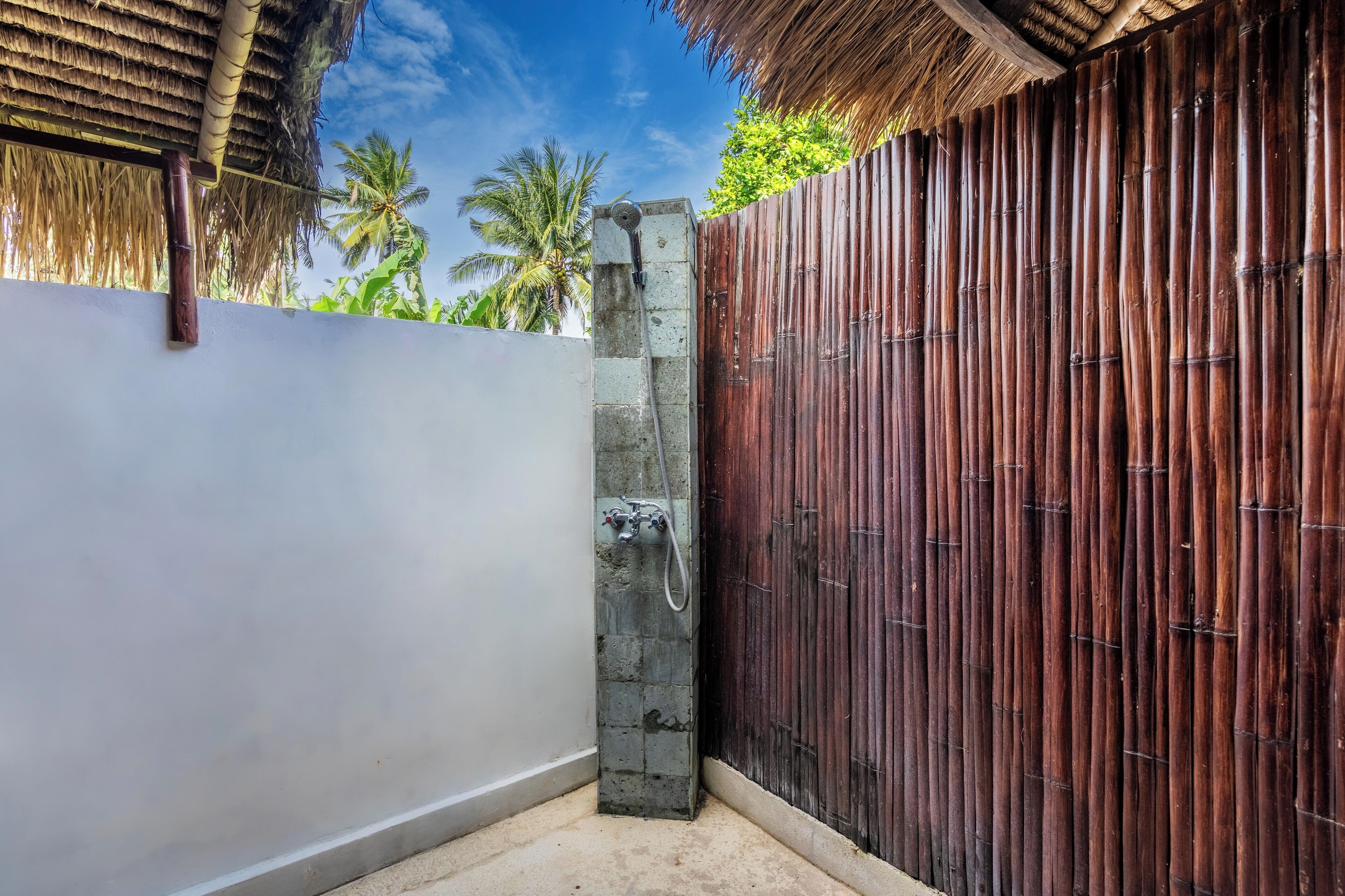 A bathroom with a concrete pillar, a shower, and a bamboo fence.