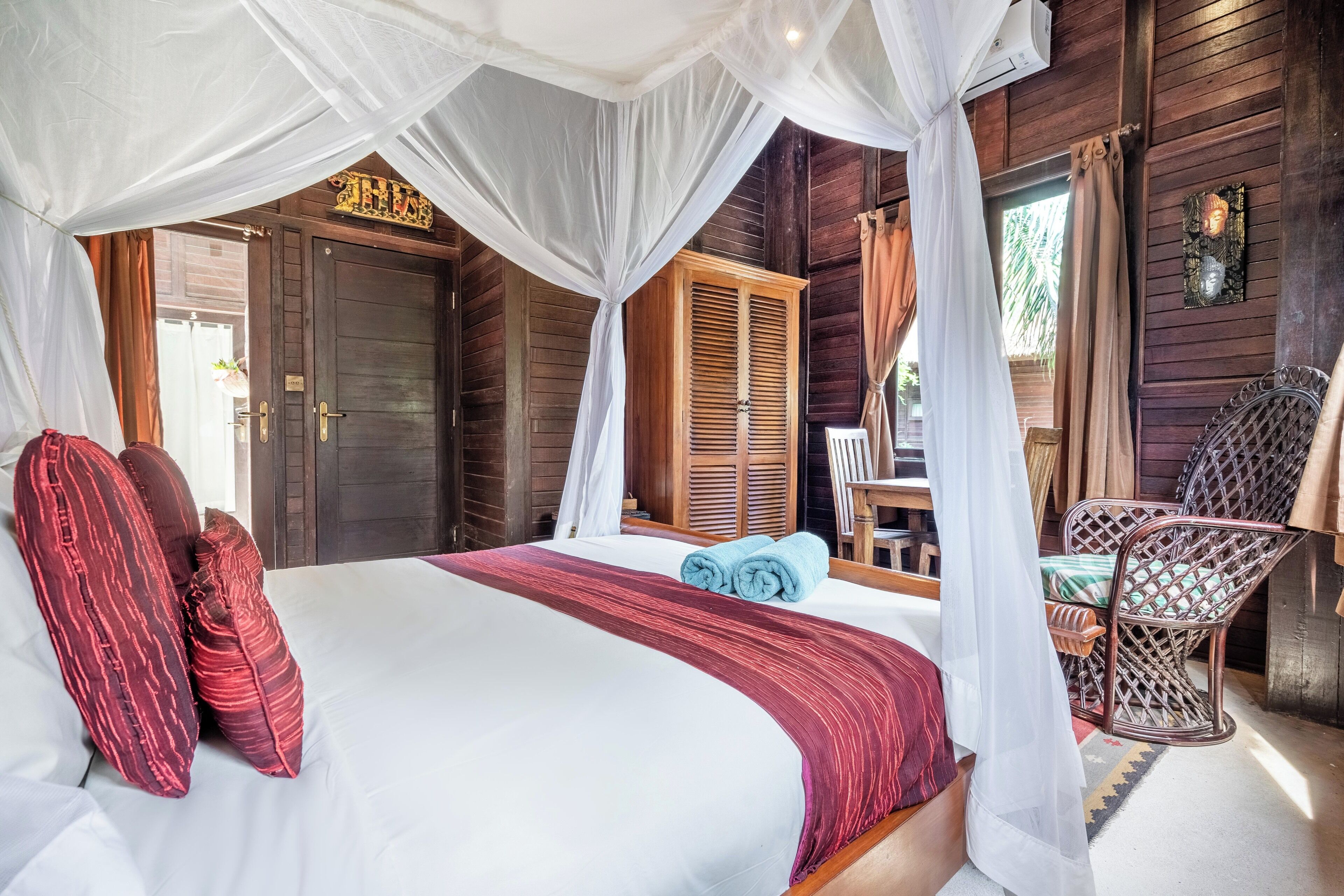 A bed with a canopy, a wooden wardrobe, and a wicker chair.
